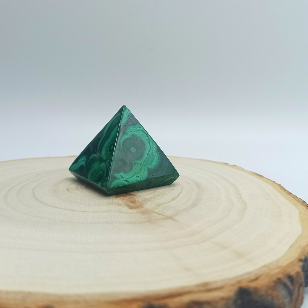 Pyramide en Malachite , posée sur un rondin de boisSon vert intense renvoie à une nature végétale vibrante. La Malachite réveille des ressentis opaques parfois clairs parfois foncés